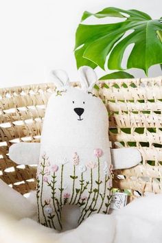 a white stuffed animal sitting on top of a bed next to a basket and plant