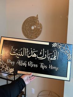 a person holding up a sign that says may alot bess this home in arabic