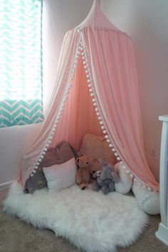 a pink tent with white pom poms and stuffed animals in it, next to a window