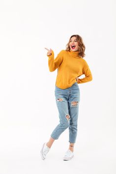 a woman wearing ripped jeans and a yellow sweater is making the peace sign with her hands