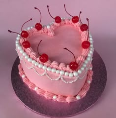 a pink heart shaped cake with cherries on top