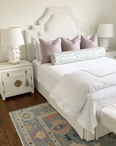 a white bed sitting in a bedroom on top of a hard wood floor next to two lamps