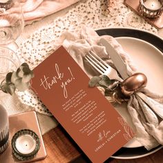 a place setting with an orange thank you card and silverware on it, next to a candle