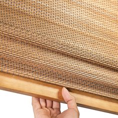 a hand is holding up the edge of a bamboo window covering that's partially closed