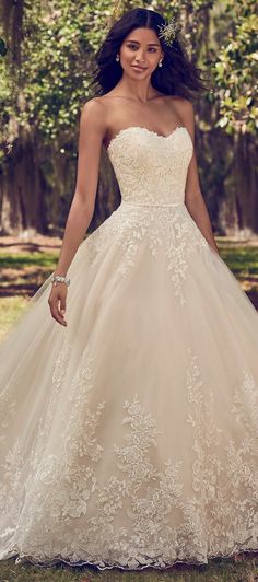 a woman in a wedding dress posing for the camera with trees in the back ground