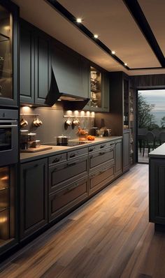 a large kitchen with wooden floors and black cabinetry is lit by recessed lighting