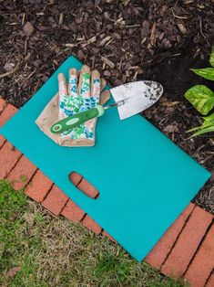 a garden tool laying on top of a blue mat next to some grass and dirt