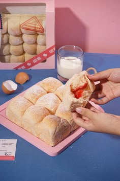 a person holding a sandwich in front of a box of doughnuts on a table