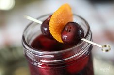 two cherries are on top of an orange slice in a mason jar with toothpicks