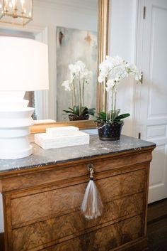 a dresser with flowers and a mirror in the background on it's side table