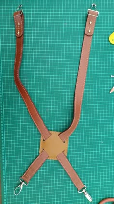 a pair of leather suspenders sitting on top of a green cutting mat next to scissors