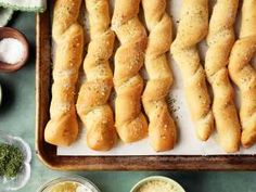 breadsticks lined up on a baking sheet with dips and seasoning in bowls