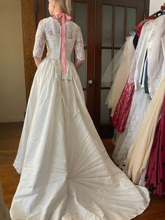 a woman standing in front of a mirror wearing a white dress and pink bow tie