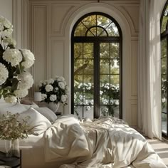 a bed with white sheets and pillows in front of an arched window that has flowers on it