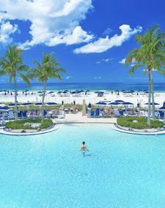 a person is swimming in the pool near palm trees and umbrellas on the beach