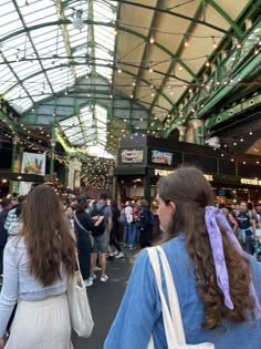 two women are walking through an indoor market with lots of people on the sidewalk and in front of them