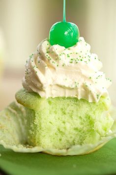 a cupcake with white frosting and green sprinkles is on a plate