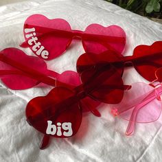 three heart shaped sunglasses with the words little big written on them sitting on a bed