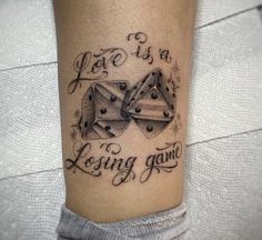 a tattoo with two dice on the leg that says, love is a losing game