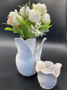 two white vases with flowers in them on a table