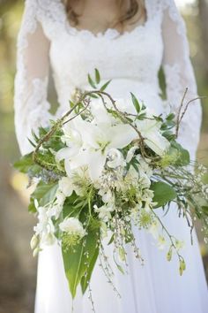 a woman in a white dress holding a bouquet of flowers and greenery on her wedding day