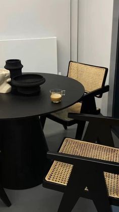 a black table with wicker chairs around it and a white wall in the background