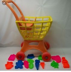 a toy shopping cart filled with plastic letters and toys on a white surface, including orange handles