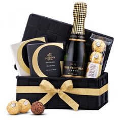 a bottle of wine, chocolates and cookies in a black gift box with gold ribbon