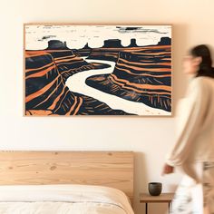 a woman walking past a bed in a room with a painting on the wall above it