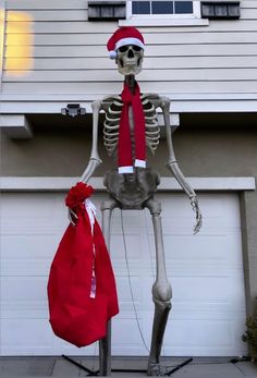 a skeleton with a santa hat and scarf standing next to a red bag in front of a house