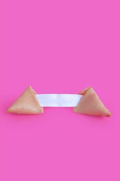 two pieces of food sitting on top of a white ribbon in front of a pink background