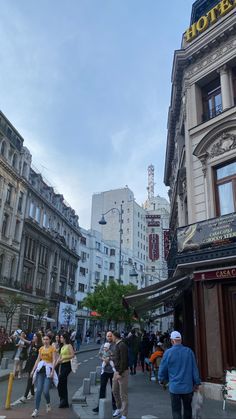 many people are walking down the street in front of some buildings and tall buildings with signs on them