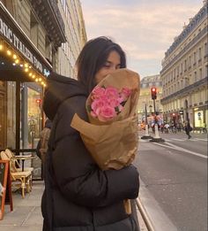 a woman is walking down the street with flowers in her hand and holding a brown paper bag