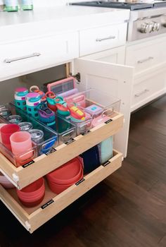 an open drawer in a kitchen filled with plastic cups and bowls on top of wooden flooring