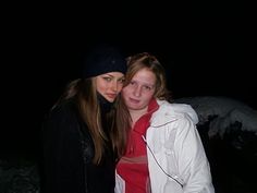 two young women standing next to each other in the snow at night with headphones on