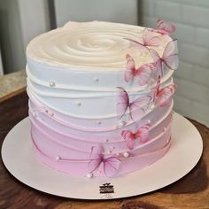 a cake with white frosting and pink butterflies on top, sitting on a wooden table