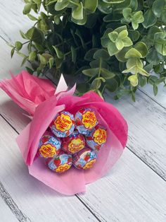 a bouquet of candy wrapped in pink paper next to a potted plant on a white wooden table