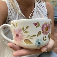 a woman holding a cup with flowers painted on it