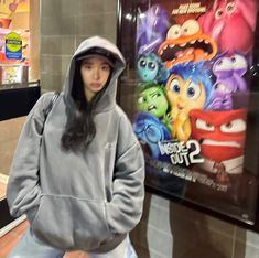 a woman standing in front of a movie poster wearing a hoodie and looking at the camera