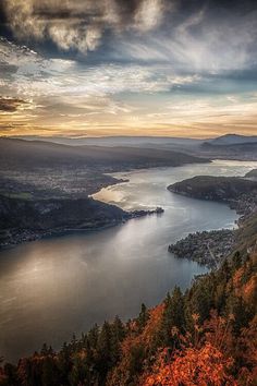 a lake surrounded by trees and mountains under a cloudy sky