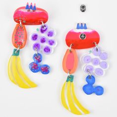 two colorful earrings are hanging from hooks on a white surface, one is shaped like a fish and the other has an octopus