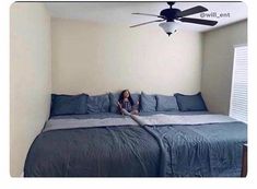 a woman sitting on top of a bed in a bedroom next to a ceiling fan