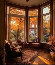 a living room filled with furniture and large windows covered in fall leaves on the trees