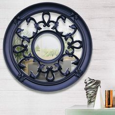 a decorative mirror hanging on the wall next to a table with vases and books