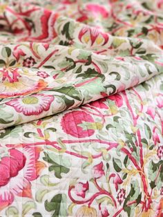 a close up view of a flowered bedspread with pink and green flowers on it