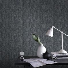 a desk with a lamp, book and other items sitting on it in front of a gray wall