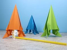 three origami airplanes sitting on top of a table next to a yellow pencil