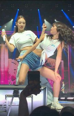 two girls are performing on stage with their cell phones