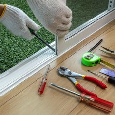 a person with gloves and tools on their feet near a window sill that has grass in the background