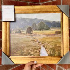 a person holding up a painting in front of a brick wall